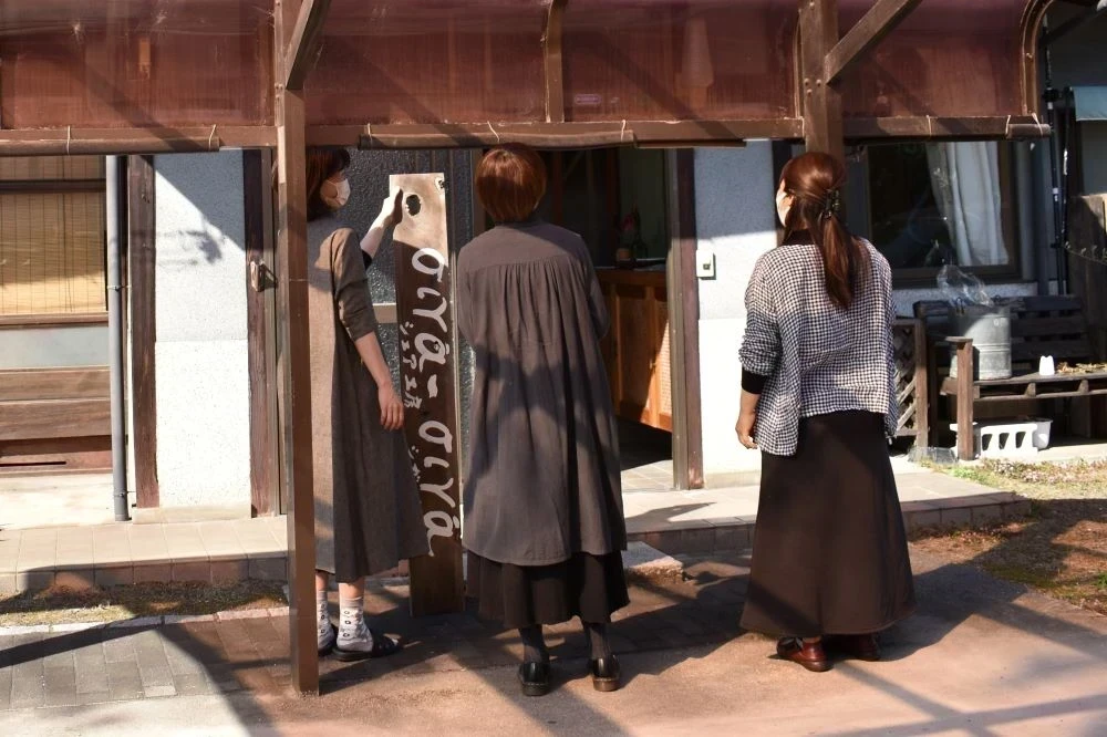 看板をどこにかけようか相談する3人